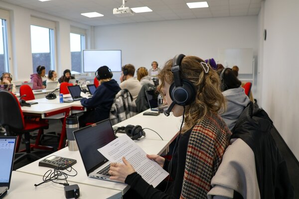 Ein Klassenzimmer der WDS Ein Klassenzimmer voller junger Erwachsener, die alle ein Headset tragen und vor ihrem Laptop sitzen.